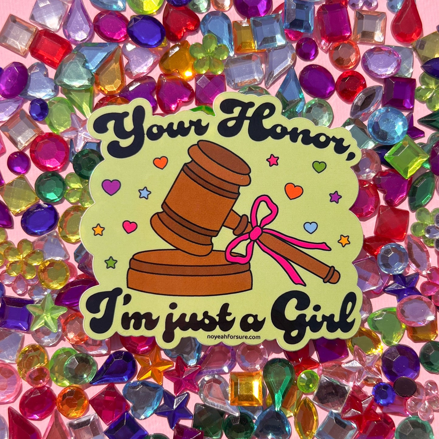 Sticker featuring a judge's gavel with a pink bow and the whimsical text, "your honor, i'm just a girl" surrounded by colorful hearts and stars on a colorful
background with gems.