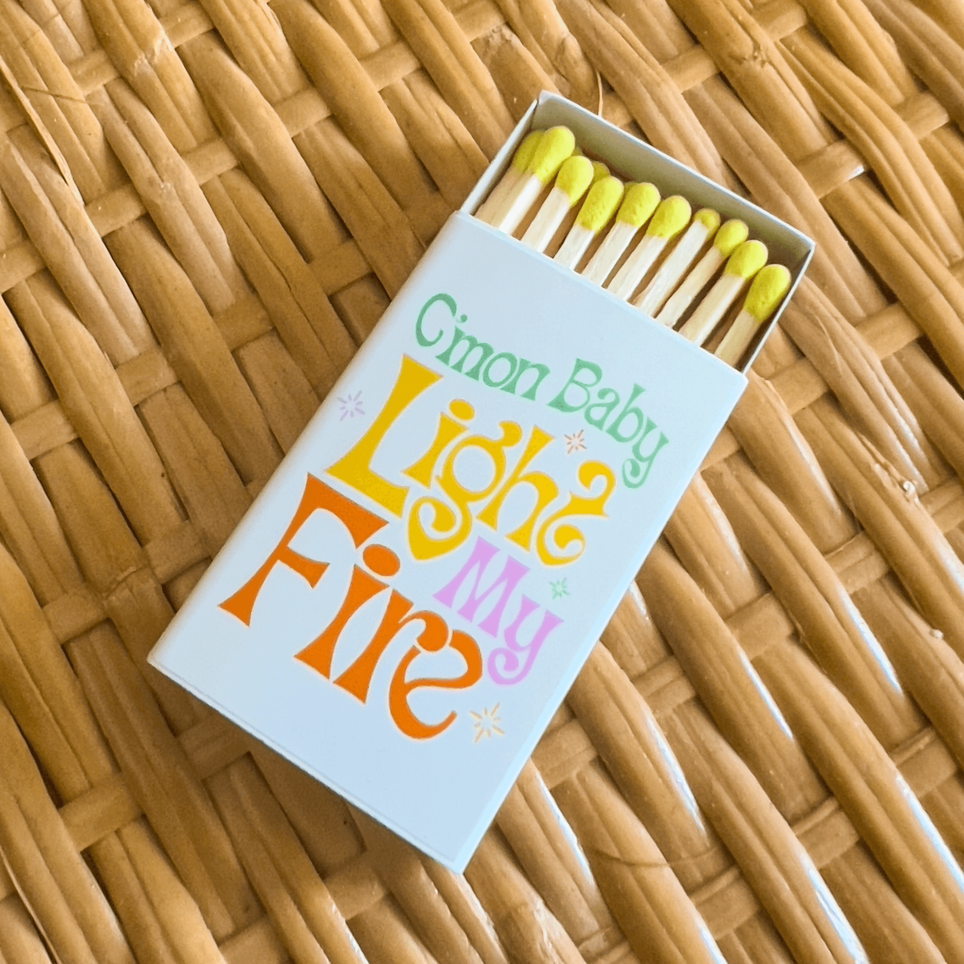 Matchbox on wicker table with come on baby light my fire text graphic. Yellow tipped matches