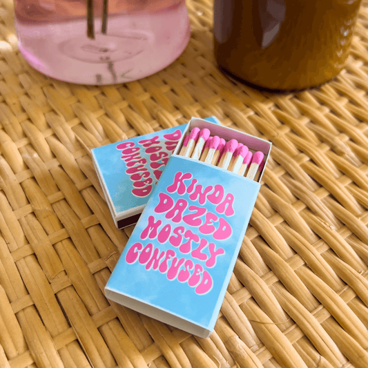 Matchbox on a wicker table with pink tipped matches.Sky cloud graphic with kinda dazed mostly confused text