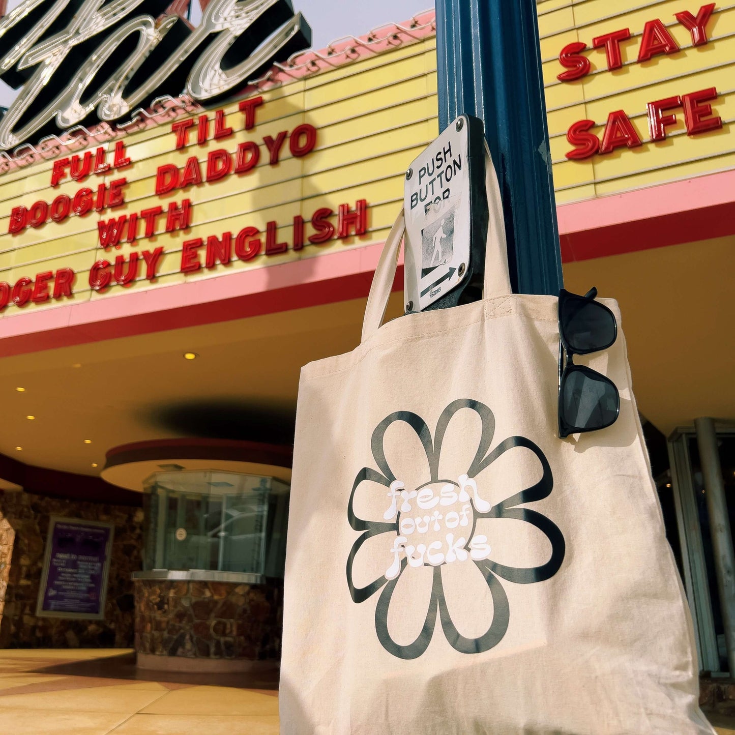 fresh out of fucks black flower tote bag on cross walk sign in front of theatre