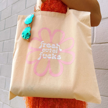 fresh out of fucks tote bag with pink flower in front of white brick wall